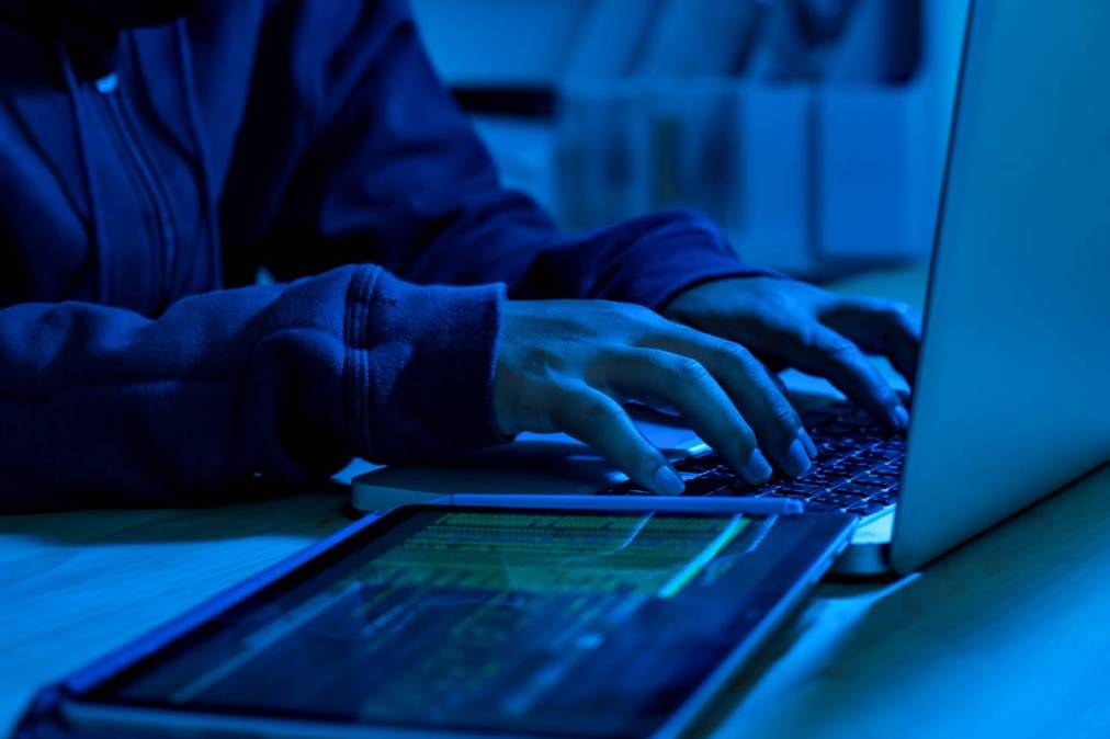 Photograph of a man typing wearing a hoodie, the photograph has a moody, blue filter.